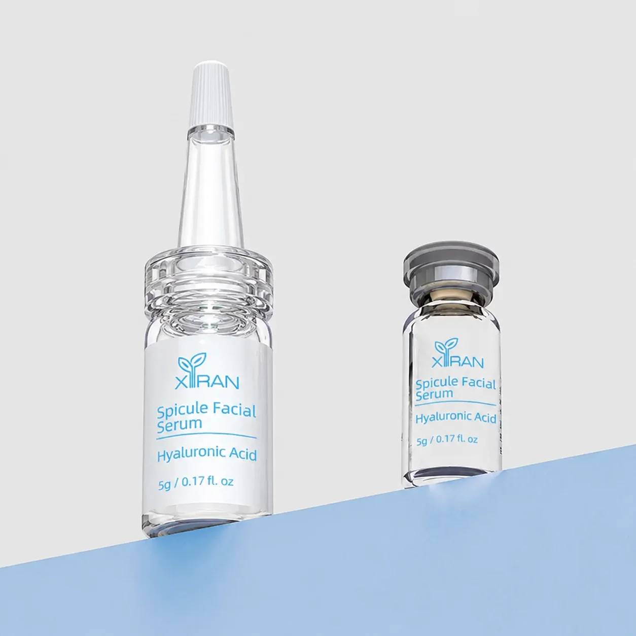 Two XIRAN spicule facial serum bottles containing hyaluronic acid, displayed on a blue and gray background. Labels are clearly visible.